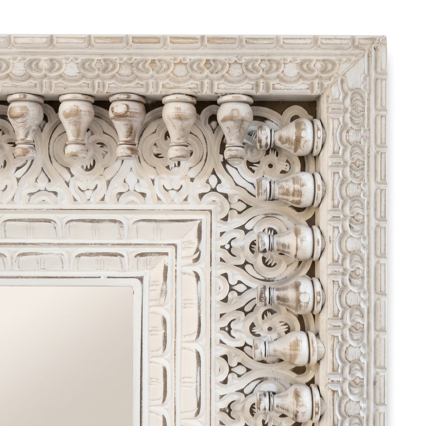 Detalle del marco tallado y calado a mano del espejo, con balaustres torneados y relieve floral en blanco envejecido
