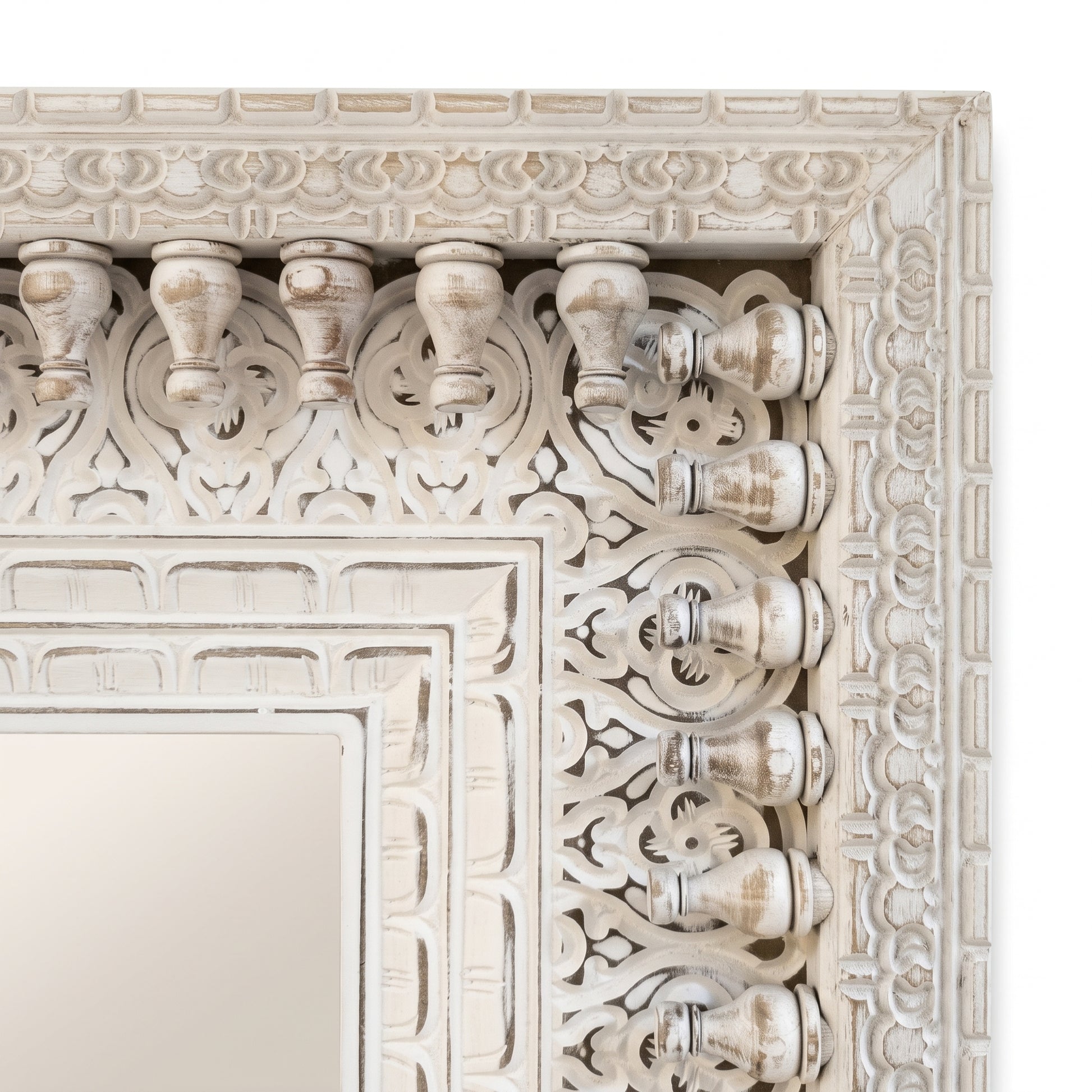 Detalle del marco tallado y calado a mano del espejo, con balaustres torneados y relieve floral en blanco envejecido