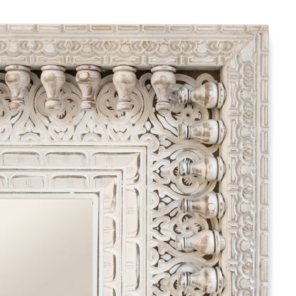 Detalle del marco tallado y calado a mano del espejo, con balaustres torneados y relieve floral en blanco envejecido