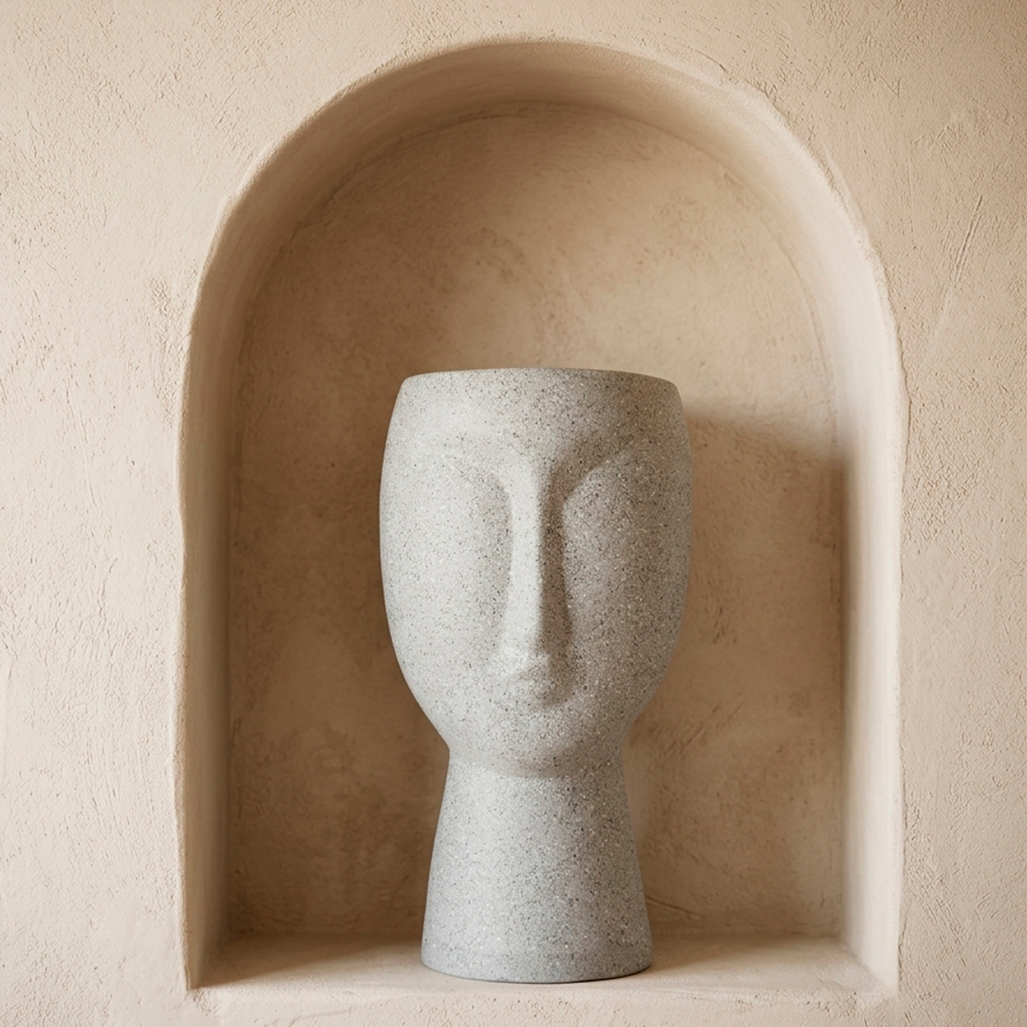 Matera decorativa con forma de rostro en cerámica gris moteado efecto piedra, dentro de un nicho de pared cálido