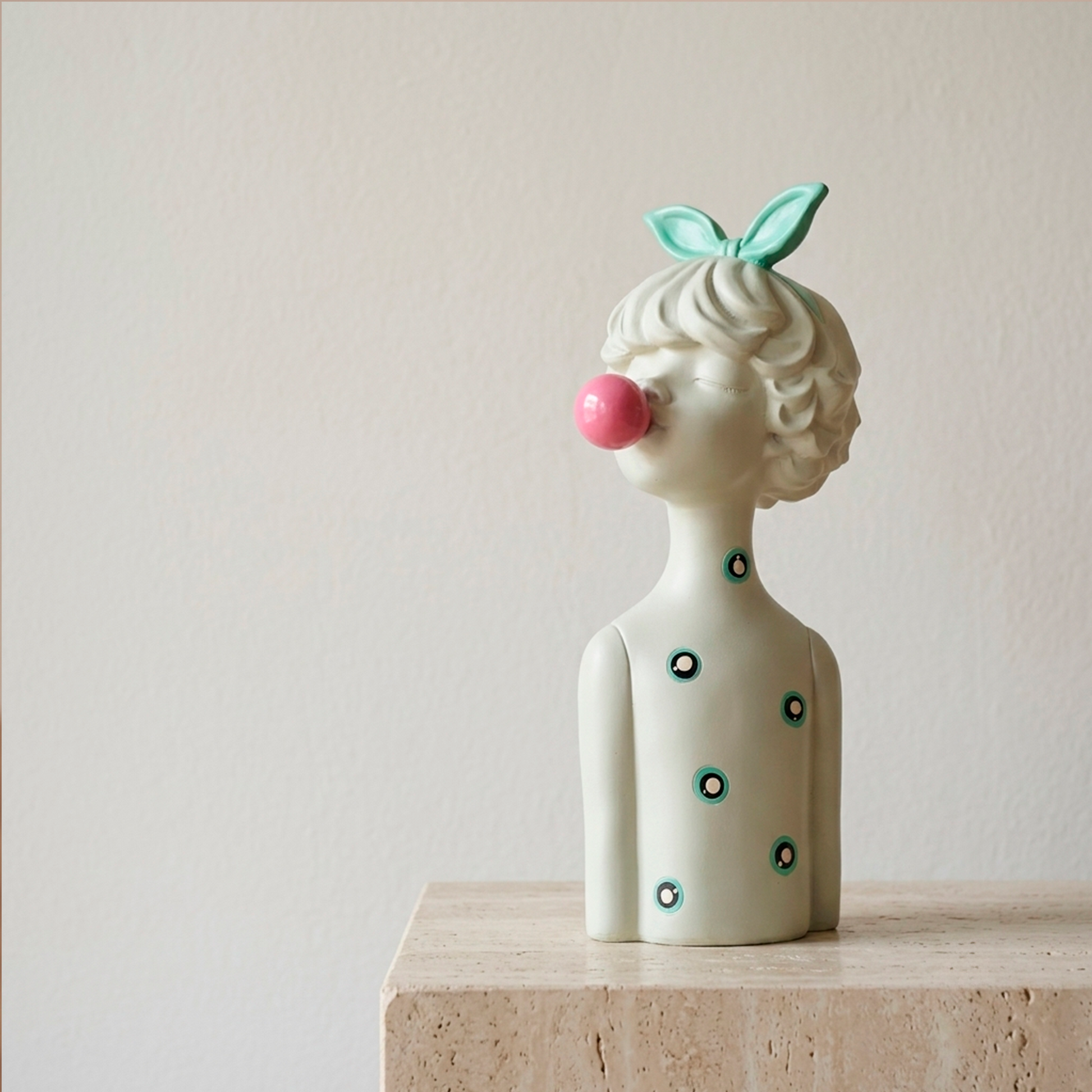 Figura decorativa de niña con lazo agua marina soplando un globo de chicle rosado, en resina blanca con detalles turquesa, sobre fondo blanco