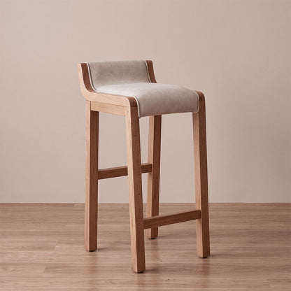 Silla de barra Artesana en roble natural con asiento tapizado en poliéster tipo cuero marfil, vista diagonal en ambiente cálido