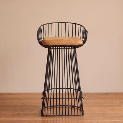 Silla de barra en varilla metálica negra con asiento coñac y descansapiés integrado, vista diagonal en ambiente cálido