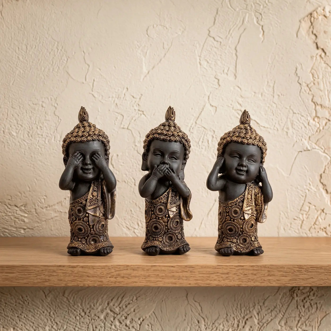 Set de tres figuras de Budas sabios en resina color carbón y bronce sobre repisa de madera clara.
