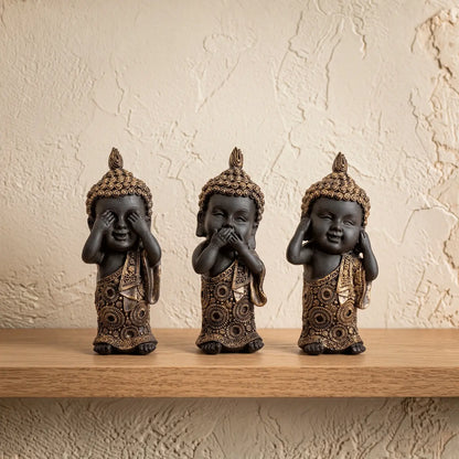 Set de tres figuras de Budas sabios en resina color carbón y bronce sobre repisa de madera clara.